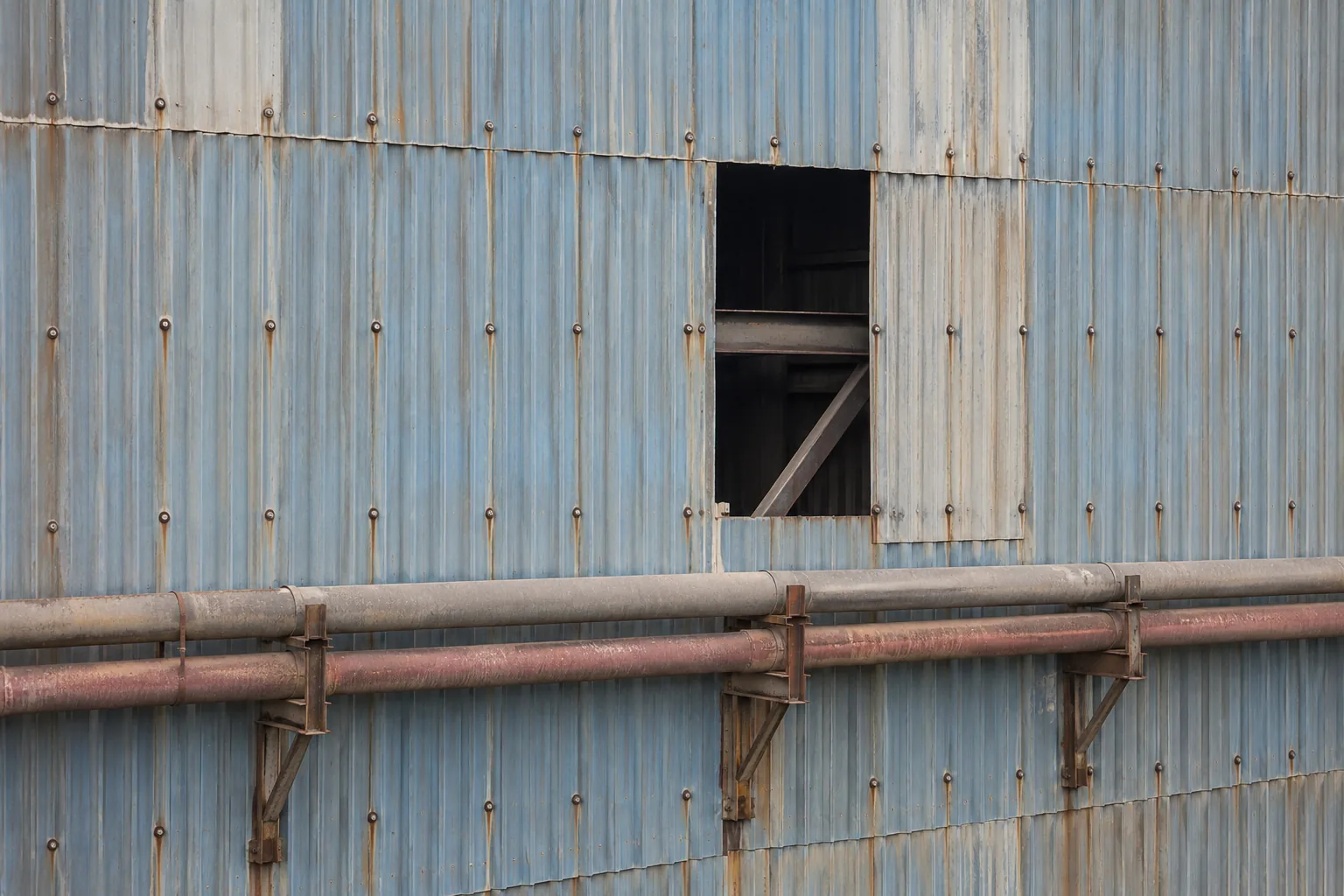 A missing cladding sheet leaves a dark rectangular opening in a corrugated wall